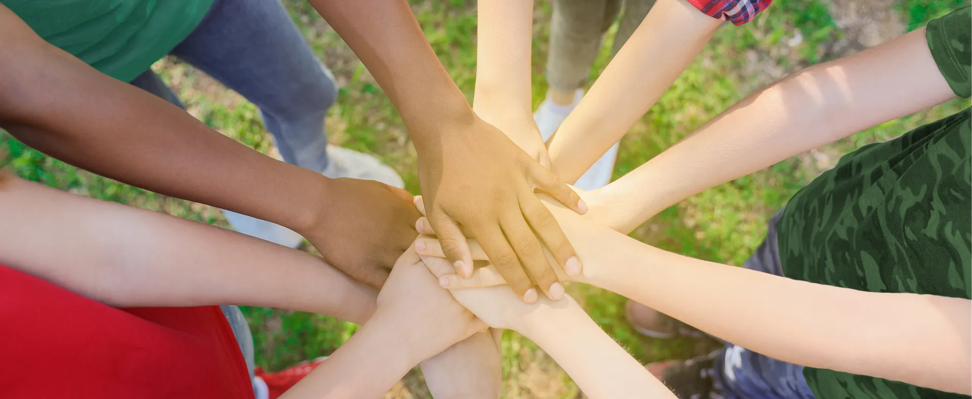Vue en plongée sur des mains de cinq enfants qui forment un cercle. Leurs mains sont posées les unes par-dessus les autres au centre du cercle.