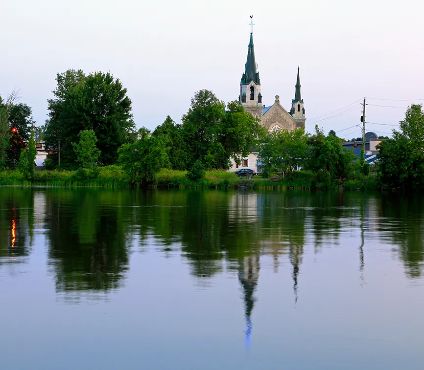 Photo de l’église d’Hawkesbury, aperçue entre les arbres depuis la rivière des Outaouais.