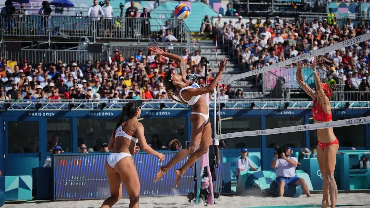 Devant une foule qui les observe depuis les estrades, trois femmes en bikini jouent au volleyball de plage.