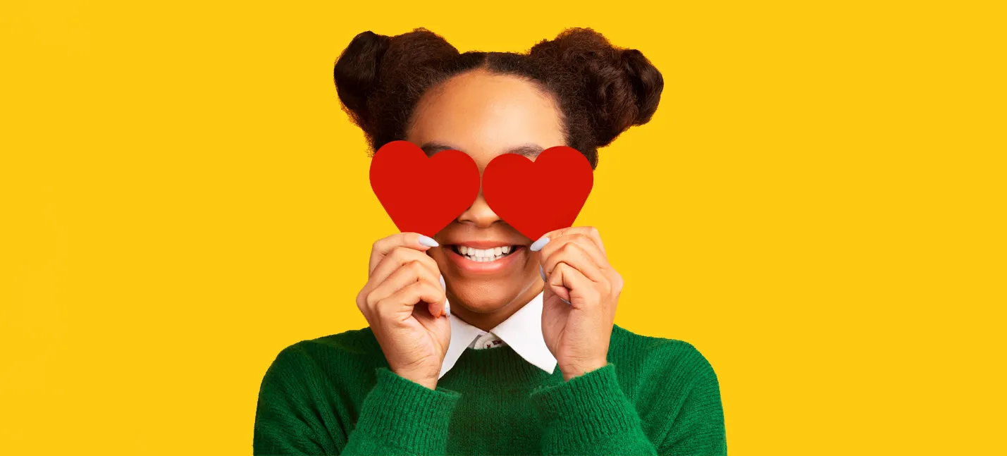 Photo d’une adolescente qui tient deux cœurs en carton rouge devant ses yeux.